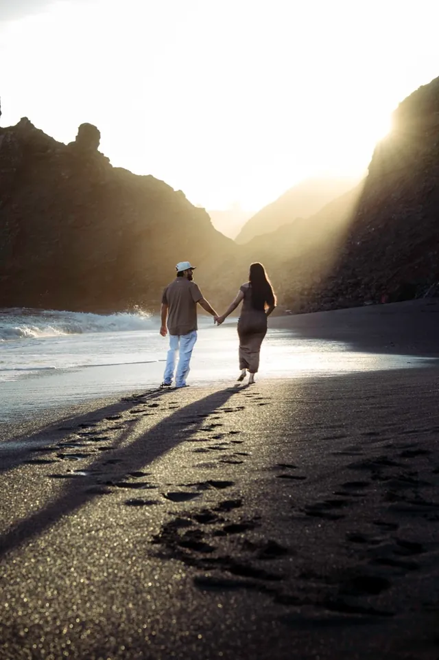 Couple walking hand in hand along the shoreline, leaving footprints in the sand.