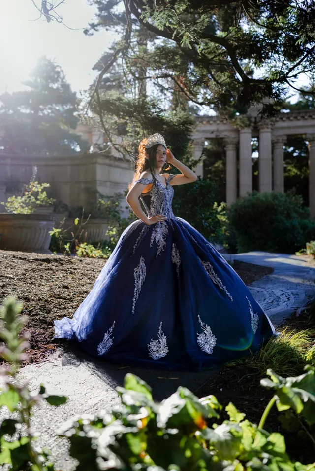 Quinceañera in an embroidered navy ball gown before classical columns.