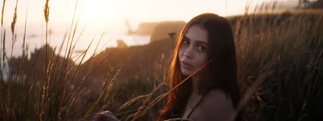 Cinematic portrait looking back through tall grass on a coastal cliff.