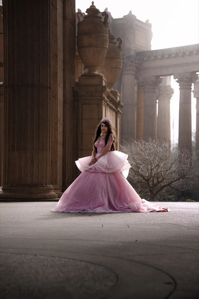 Quinceañera in a pink ruffled ball gown and tiara among the columns of a classical rotunda.
