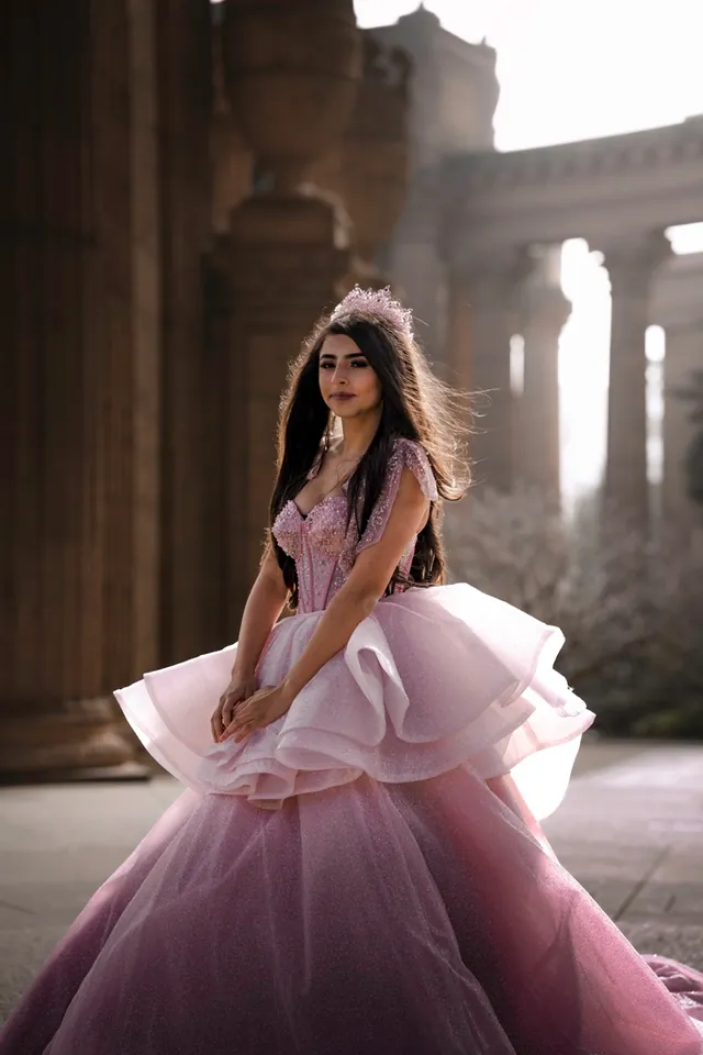 Close portrait of a quinceañera in a beaded pink gown and tiara, backlit by soft morning haze.